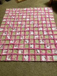 a pink and green patchwork quilt on the floor in a room with carpeting