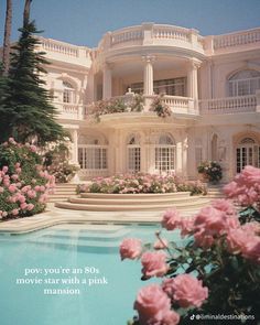 a large white house with pink flowers in the foreground and a pool surrounded by trees