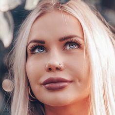 a woman with long blonde hair and blue eyes is posing for a photo in front of some trees