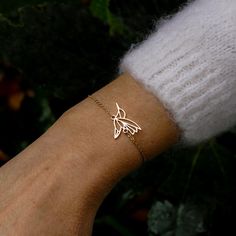 a woman's arm with a gold bracelet that has a small bird on it