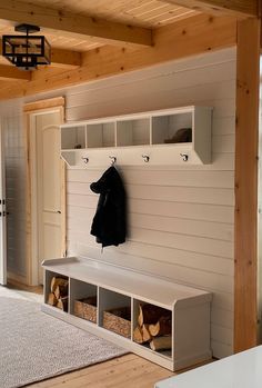 a coat rack and bench in a room with wood flooring, white walls and wooden beams