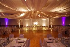 a banquet hall decorated with white linens and purple uplighted draping