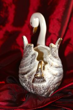 a white swan shaped vase sitting on top of a red cloth