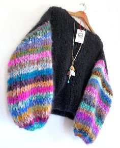 a multicolored sweater hanging on a wooden hanger next to a necklace and earring