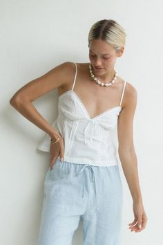 The Ezra Woven Cotton Cami Tank features a sweet babydoll style. Its smocked back, front tie, and delicate eyelet details make this the sweetest top to wear this summer. Spring Linen Tops With Smocked Bodice, Feminine Vacation Tops With Tie Straps, Feminine Tie Strap Tops For Vacation, Broderie Anglaise Tops For Summer Beach, Feminine Tie Back Tops For Daywear, Summer Beach Tops With Broderie Anglaise, Chic Linen Top With Smocked Bodice, Feminine Beach Tops With Tie Straps, Feminine Tops With Tie Straps For The Beach