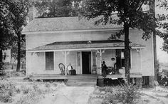 an old black and white photo of two people sitting on the porch of a house