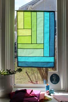 a window with a green, blue and yellow quilt hanging from it's side