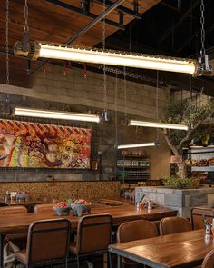 an empty restaurant with wooden tables and hanging lights above the dining area, along with art work on the wall