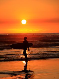 a man holding a surfboard while standing on top of a beach next to the ocean