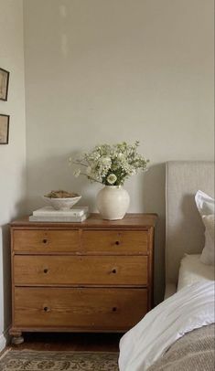 a white vase sitting on top of a dresser next to a bed in a bedroom