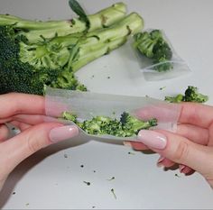 two hands holding a knife with broccoli on it