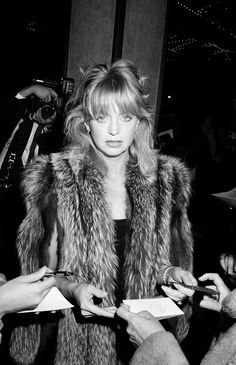 a black and white photo of a woman in fur coat signing autographs for people