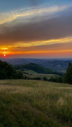 the sun is setting over some hills and fields with trees in the foreground, as seen from an overlook point