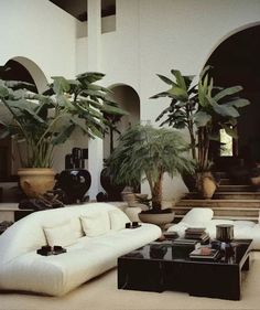 a living room filled with white furniture and potted plants on top of each other