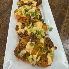 three stuffed peppers with cheese and green onions on a white platter sitting on a wooden table