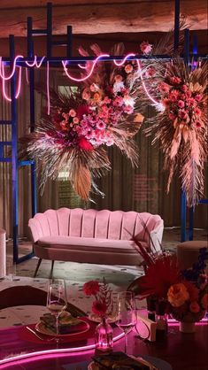 a pink couch sitting under a neon sign next to a table with flowers on it