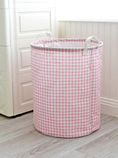 a pink and white checkered laundry hamper sitting on the floor next to a window