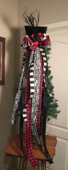 a christmas tree with black and red ribbons on it's top, sitting in the corner of a room