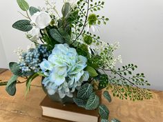 a vase filled with flowers and greenery sitting on top of a wooden table next to a book