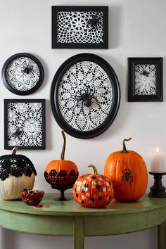 a green table topped with pumpkins next to pictures on the wall and candles in front of them