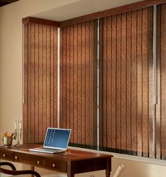 a laptop computer sitting on top of a wooden desk next to a window covered in blinds