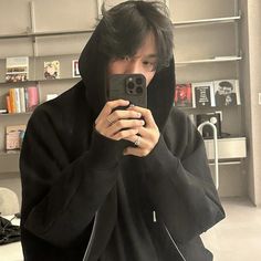 a man in a black hoodie taking a selfie with his cell phone while wearing a hooded jacket