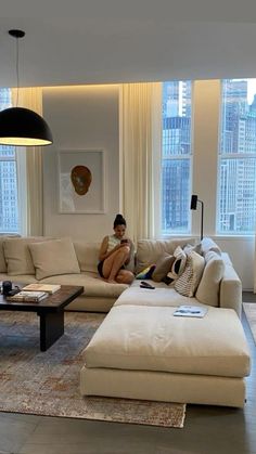 a woman sitting on a couch in a living room next to a window with large windows