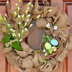 a burlap wreath with eggs and flowers on the front door is decorated with greenery