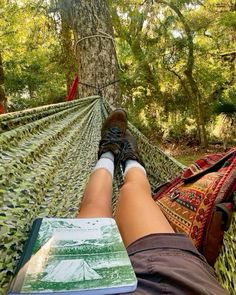 a person laying in a hammock with their feet propped up on a book