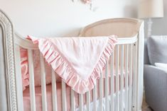 a white crib with pink bedding and pillows