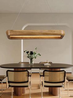 a dining room table with chairs and a plant in the center, suspended light over it