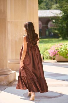 a woman in a brown dress is standing outside