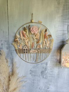 a wall hanging with flowers on it next to a candle and some dried grass in front of a clock