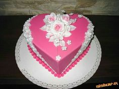 a pink heart shaped cake with white flowers on the top and bottom, sitting on a plate