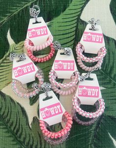 pink and white bracelets with name tags on them sitting next to some green leaves