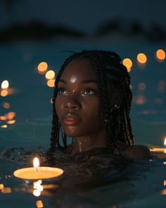 a woman is in the water with candles floating around her and looking at the camera