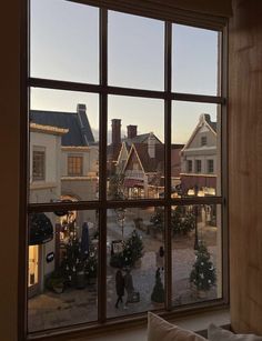 the view from an open window looking out onto a town square with christmas trees and shops