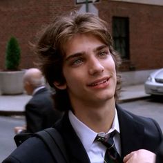 a young man in a suit and tie standing on the street looking off into the distance