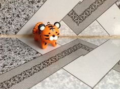 a small orange tiger figurine sitting on top of a tile floor next to a wall