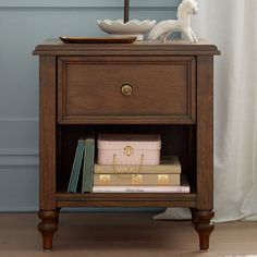 a wooden table with books and a lamp on it's side stand next to a mirror