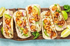 shrimp tacos with avocado and cilantro on a cutting board next to lime wedges