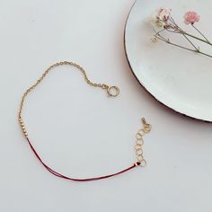 Close-up of hand wearing delicate bracelet of gold chain and red thread with gold beads detail at center. Adjustable Rose Gold Bracelet With Satellite Chain, Adjustable Minimalist Satellite Chain Bracelet, Gold Beaded Chain Friendship Bracelets As Gift, Minimalist Beaded Bracelet With Adjustable Chain, Adjustable Gold Beaded Chain Friendship Bracelets, Minimalist Adjustable Chain Bracelet With Tiny Beads, Minimalist Gold Beads Bracelets For Friendship, Minimalist Beaded Chain Bracelet, Minimalist Gold Beads Friendship Bracelet