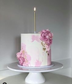 a white cake with pink flowers and a single candle