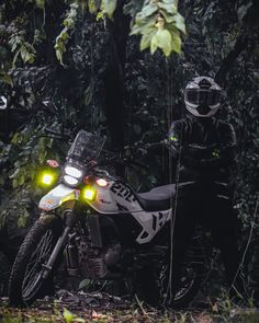 two motorcyclists are parked in the woods with their lights on and one is wearing a helmet