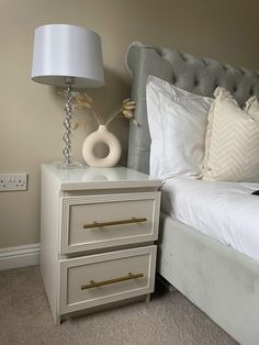 a white bed sitting next to a lamp on top of a nightstand in a bedroom