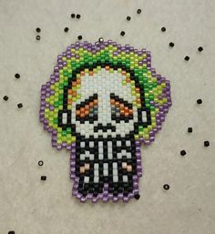 a beaded brooch with an image of a skeleton wearing a clown mask on it's head