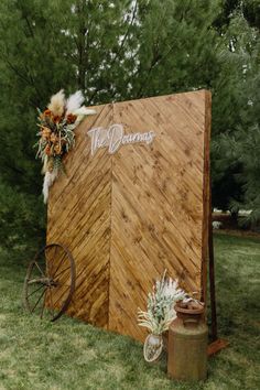 a wooden sign sitting on top of a lush green field next to a metal barrel