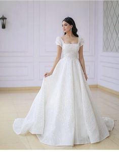 a woman in a white wedding dress standing on the floor with her hands behind her back