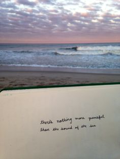 an open book with writing on it sitting in front of the beach and ocean waves