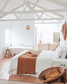 a bedroom with white walls and wood flooring has a large bed, wicker chair, and bathtub in the corner